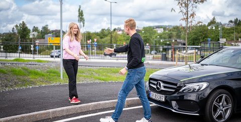 Ung mann hilser på ung kvinne foran en bil